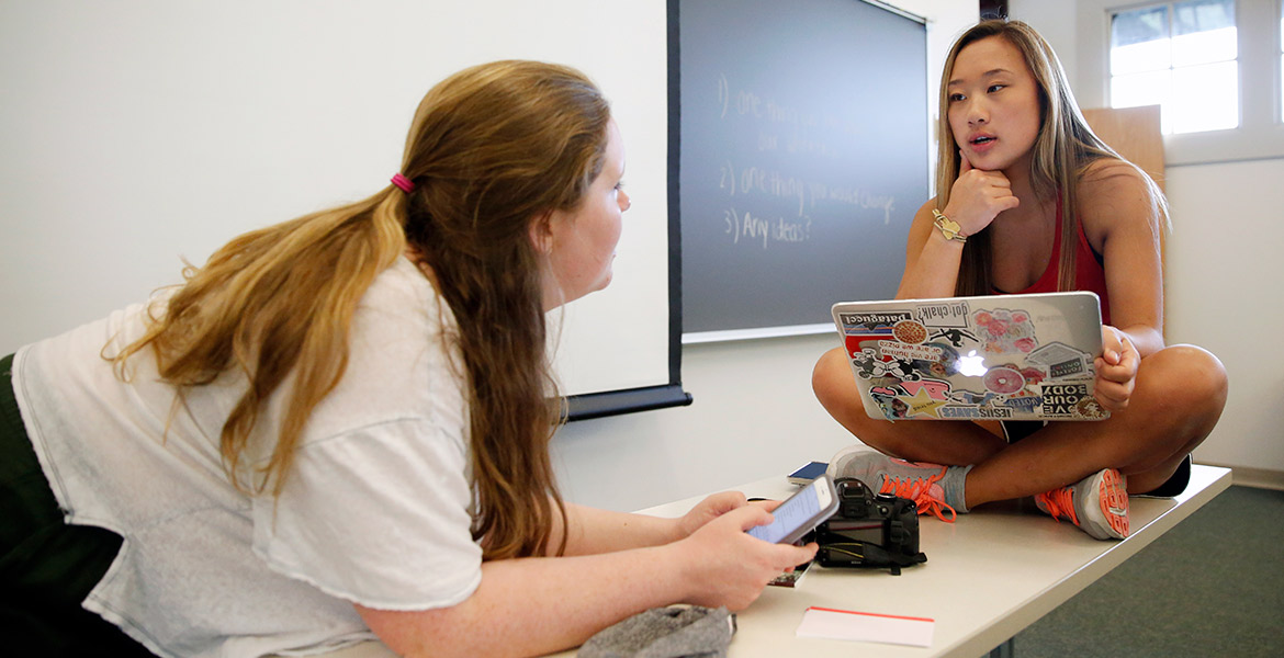 Brown and White newspaper students talking at a computer