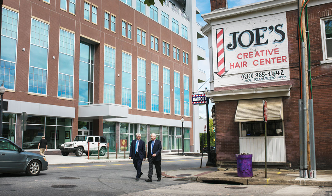 Lehigh President John D. Simon '19P and Bethlehem Mayor Robert Donchez walk between the Gateway at Greenway Park building (left) and Joe's Creative Hair Center, a South Side fixture. 