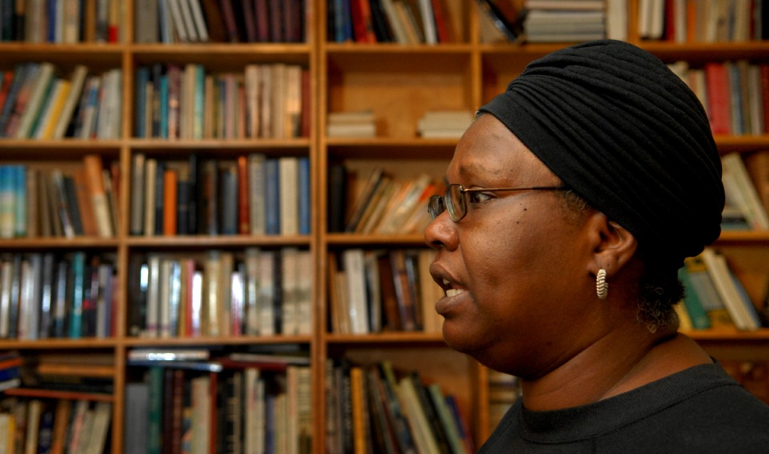 Image of writer Gloria Naylor in profile in front of bookshelf filled with books. 