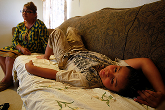 Child laying on sofa in apartment with woman on chair in background