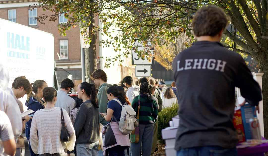 A man wearing a Lehigh sweatshirt stand in front of a line of young voters.