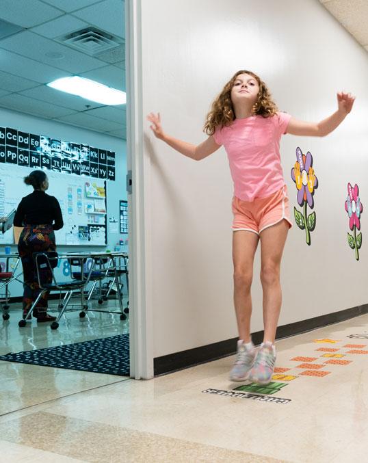 Student jumping on hopscotch board on hallway floor