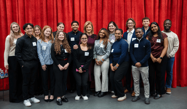 Group photo of with Arianna Huffington standing together in front of a red curtain.
