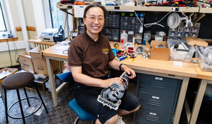 A smiling person sitting at a workbench with robotics parts, surrounded by tools and materials.