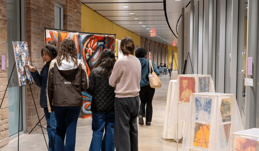 Visitors admiring colorful artworks in a gallery setting with bright lighting.