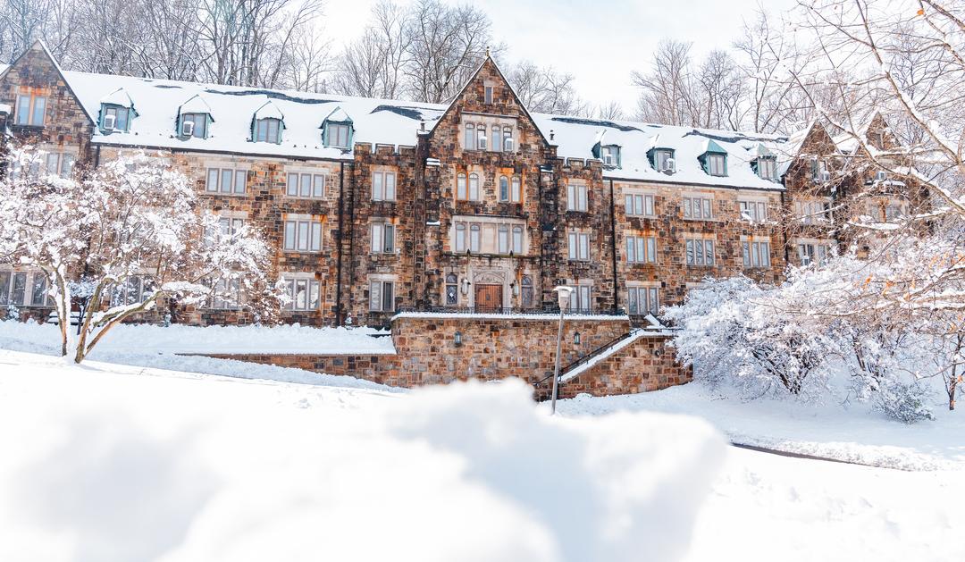 Historic stone building covered in snow, surrounded by winter trees.