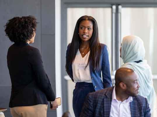 Three professionals engaged in a discussion, with varying attire and expressions, indoors.