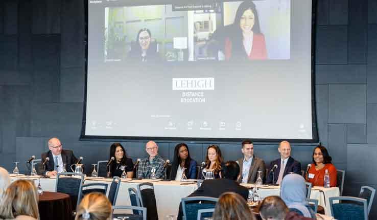 A panel discussion with eight speakers, including a video call participant in the background.
