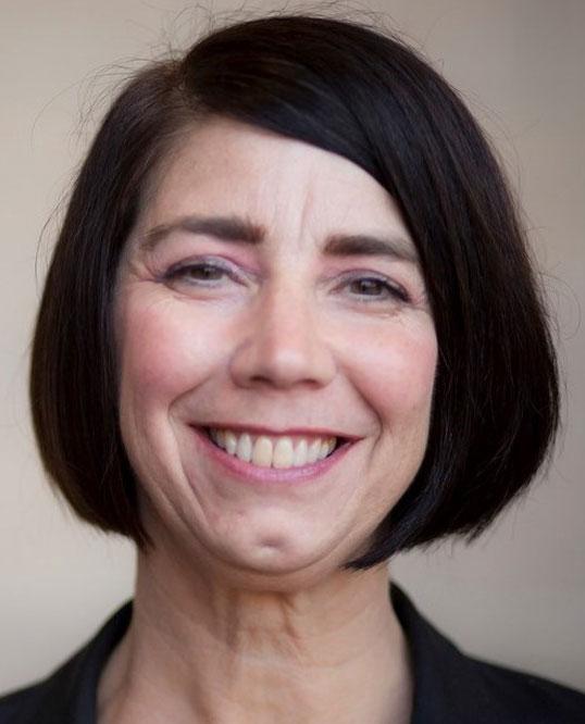 Smiling woman with short black hair and a dark blazer against a neutral background.