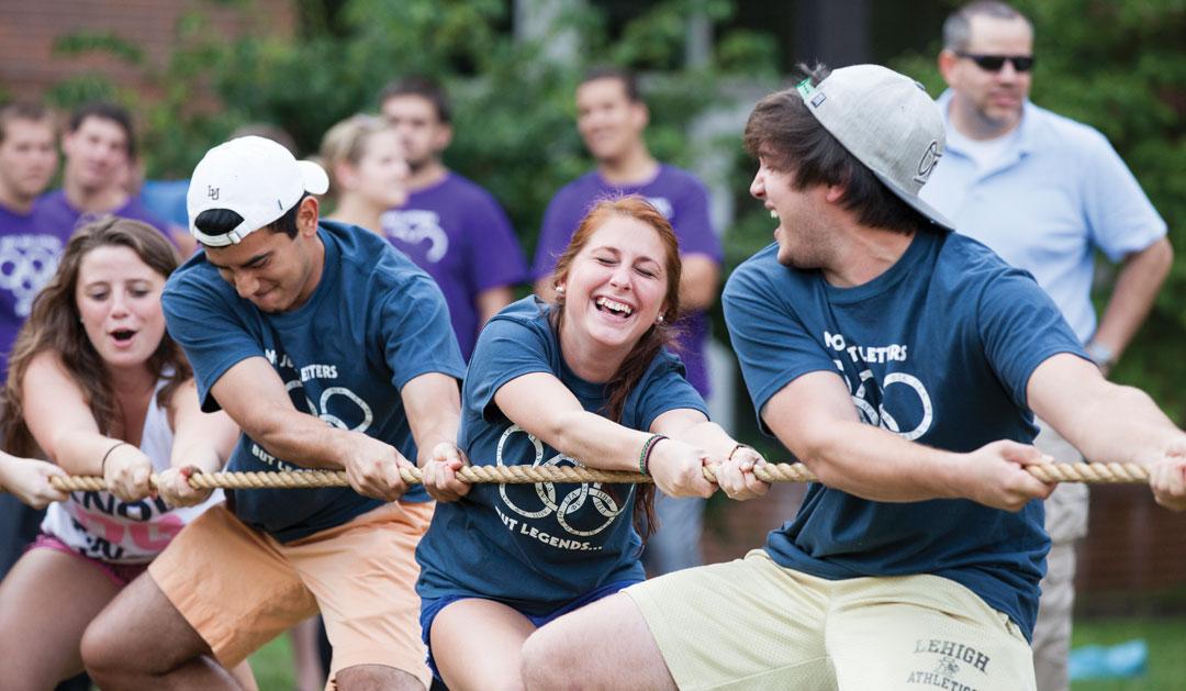 Group of four people laughing while participating in a tug-of-war event outdoors.