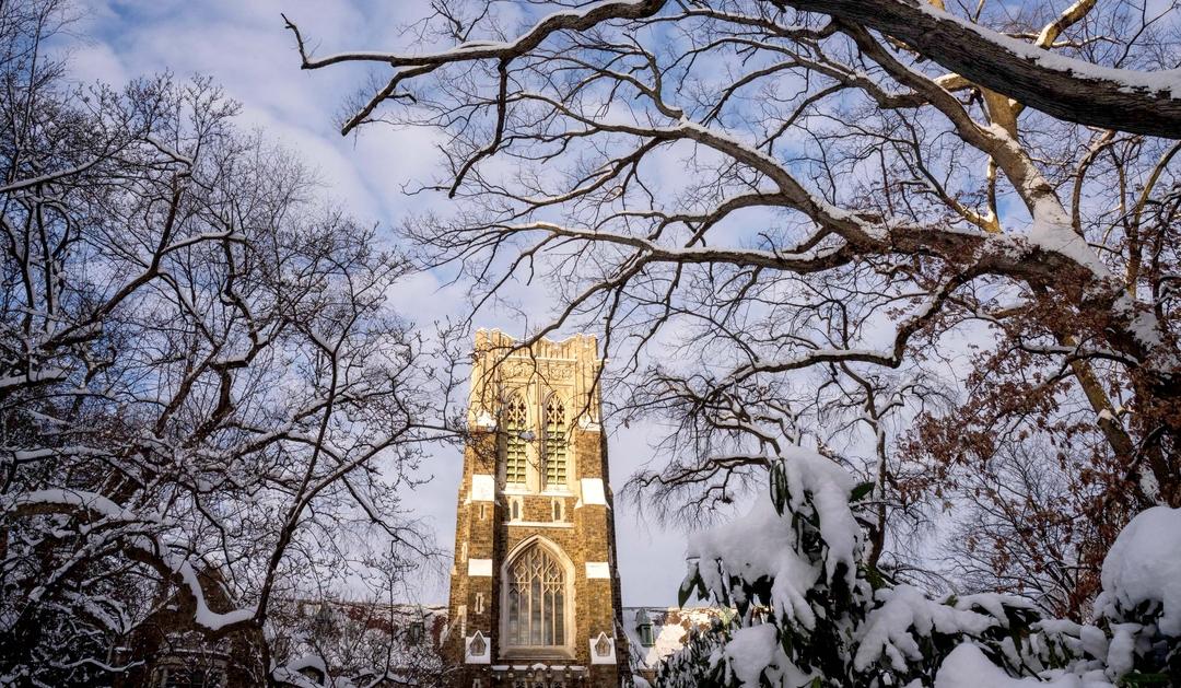 Snow-covered trees frame a tall Gothic building under a cloudy winter sky.