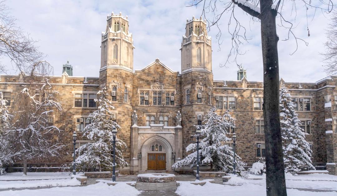 Historic stone building surrounded by snow-covered trees under a cloudy sky.