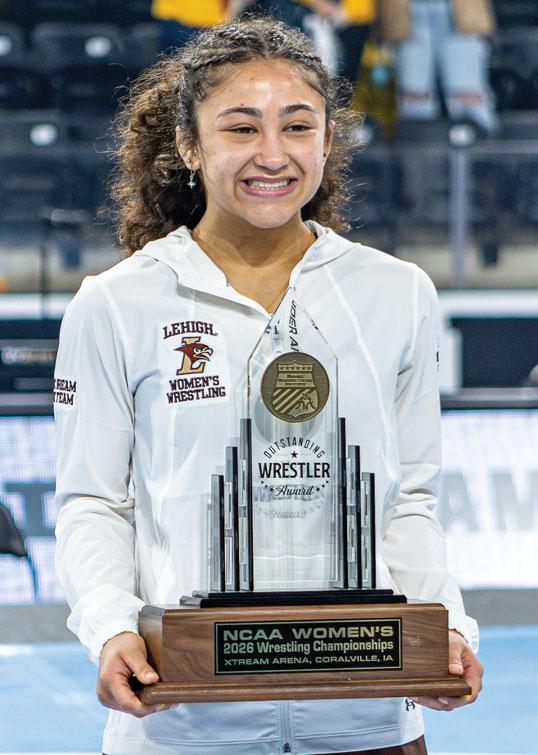 Proud female wrestler in a hoodie holds an NCAA Women's Wrestling Championship trophy.