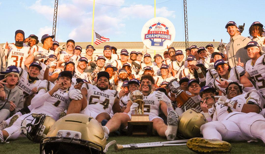 Photograph of a football team in white and gold uniforms celebrating a championship with a trophy.