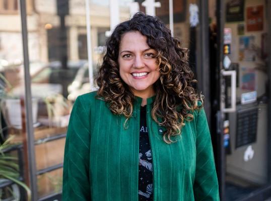 Smiling woman with curly hair in a green jacket.