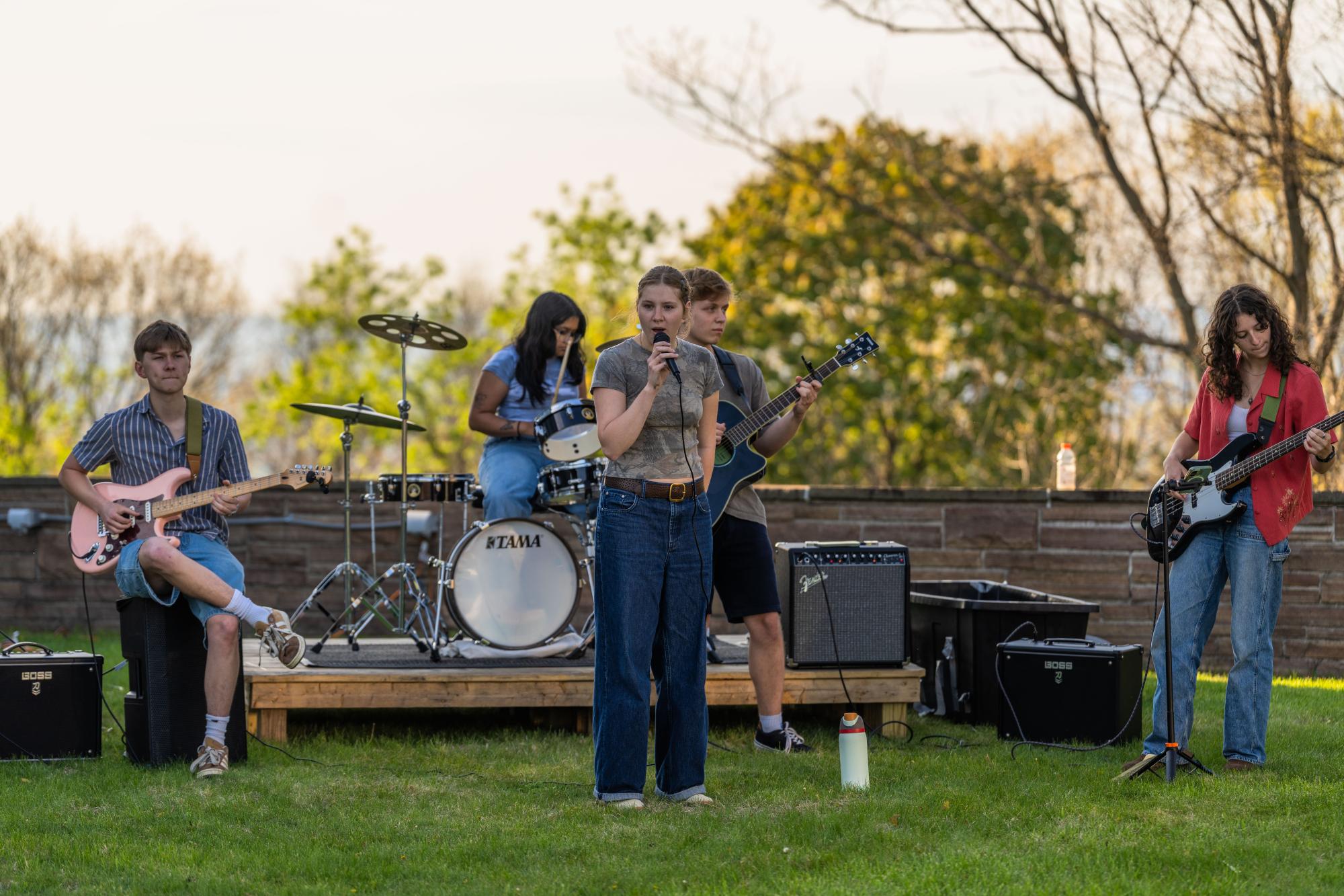 Photograph of a young five-piece band performing outdoors on a grassy field at golden hour.