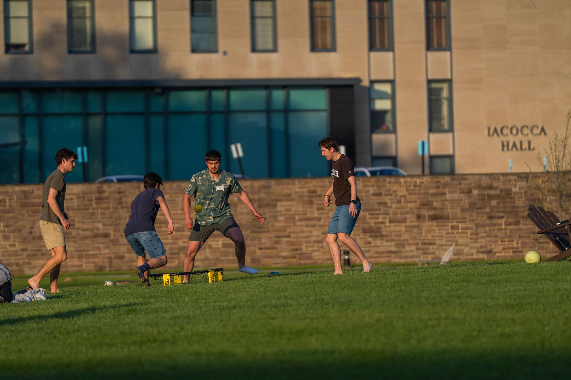Four men playing a lawn game on a green field in front of Iacocca Hall.