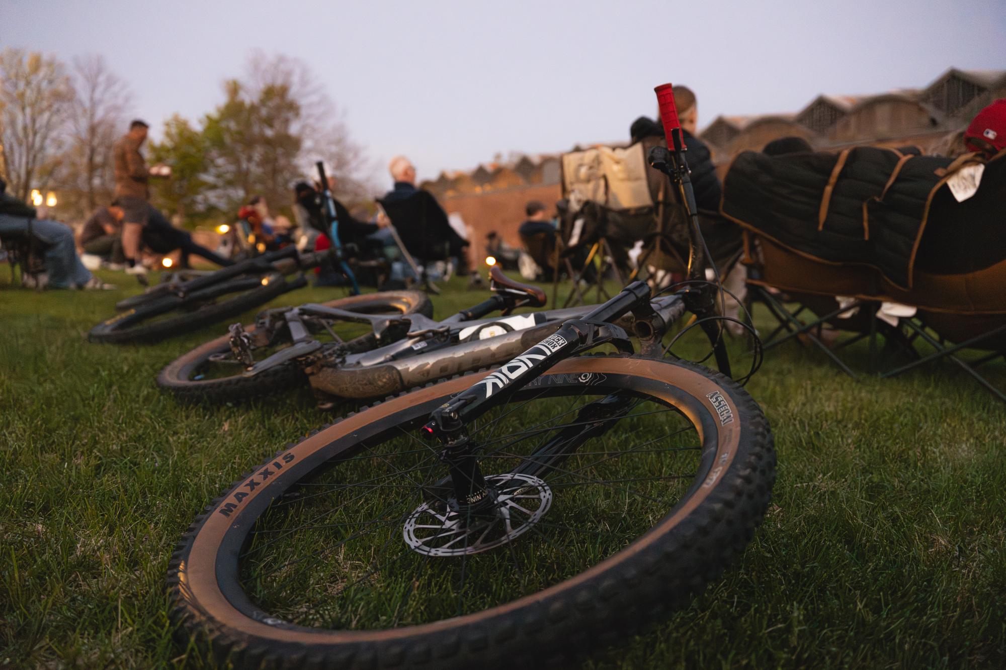 Photograph of mountain bikes on grass at an outdoor community event at dusk.