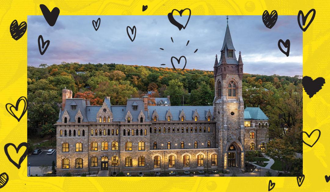 Historic stone university building with a tall spire, illuminated windows, and trees at dusk.