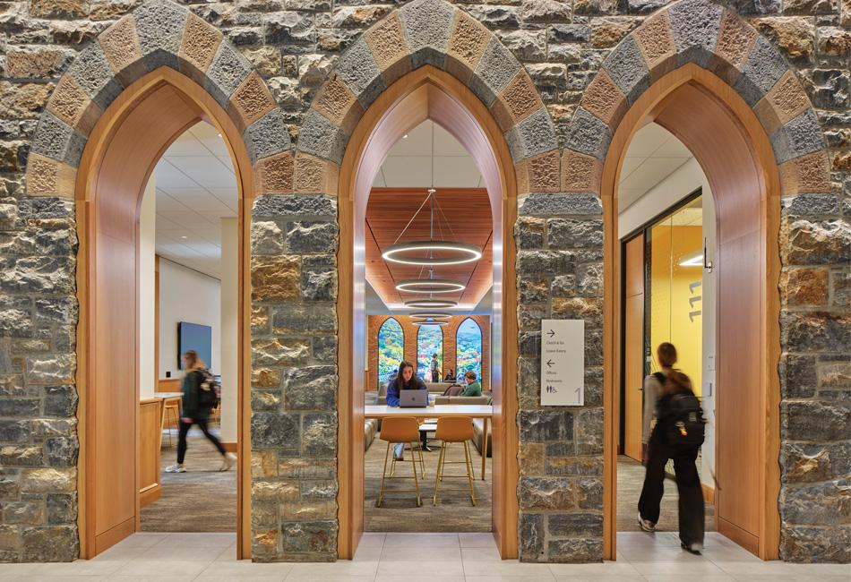 Three stone arches with wooden frames open into a bright, modern interior space. People walk inside.