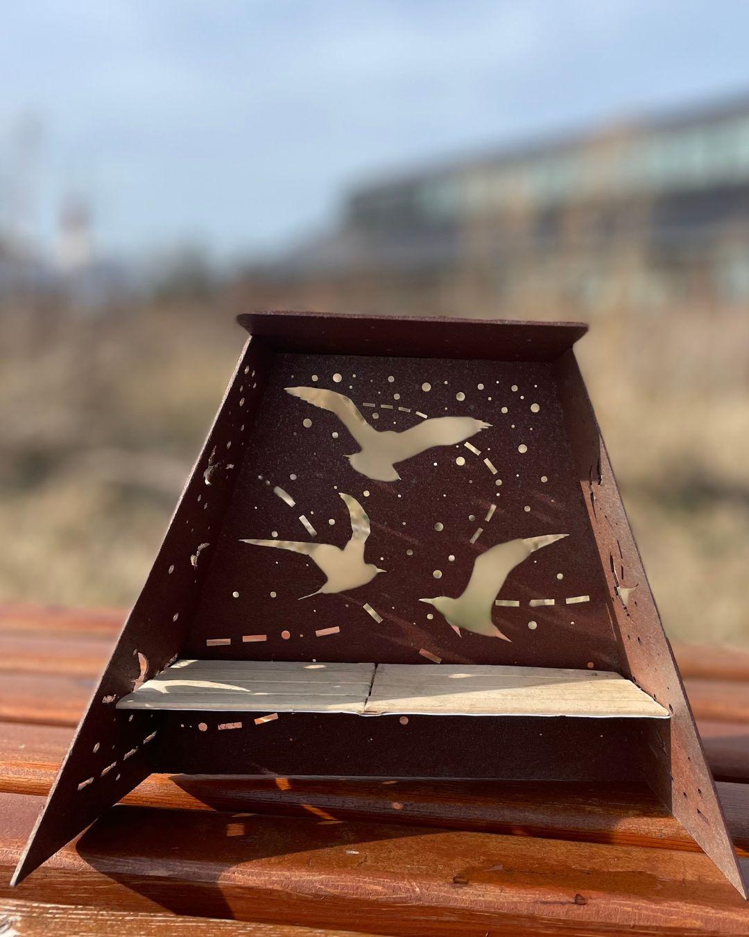 Rusted metal decorative structure with bird cutouts sitting on a wooden bench.