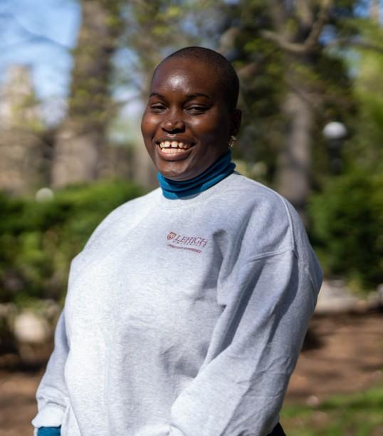 Headshot of a woman wearing a gray sweatshirt with foliage behind her on campus
