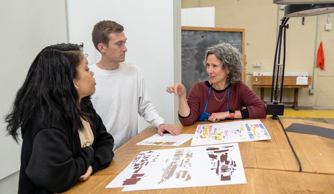 Photograph of an instructor and two students discussing design sketches in a studio.