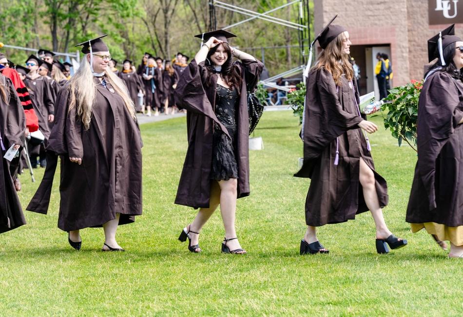 Photograph of graduates in brown gowns walking across a lawn at a Commencement ceremony.