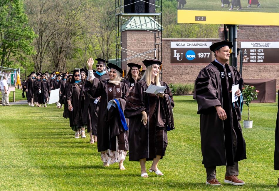Photograph of a university graduation procession with students in brown caps and gowns.