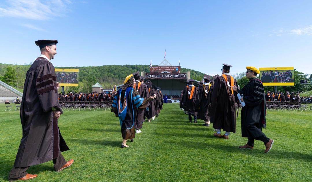 Photograph of graduates in academic regalia walking on a field at Lehigh University.