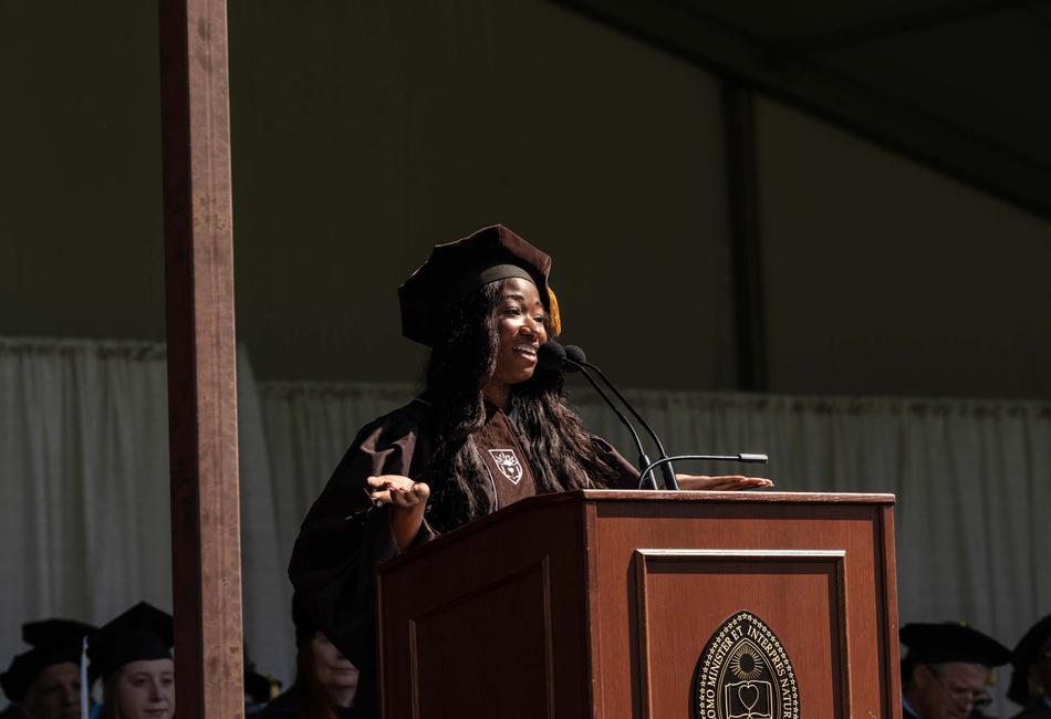Photograph of Marsha Akua Akoto Ph.D.’26 in academic regalia smiling while speaking at a podium.