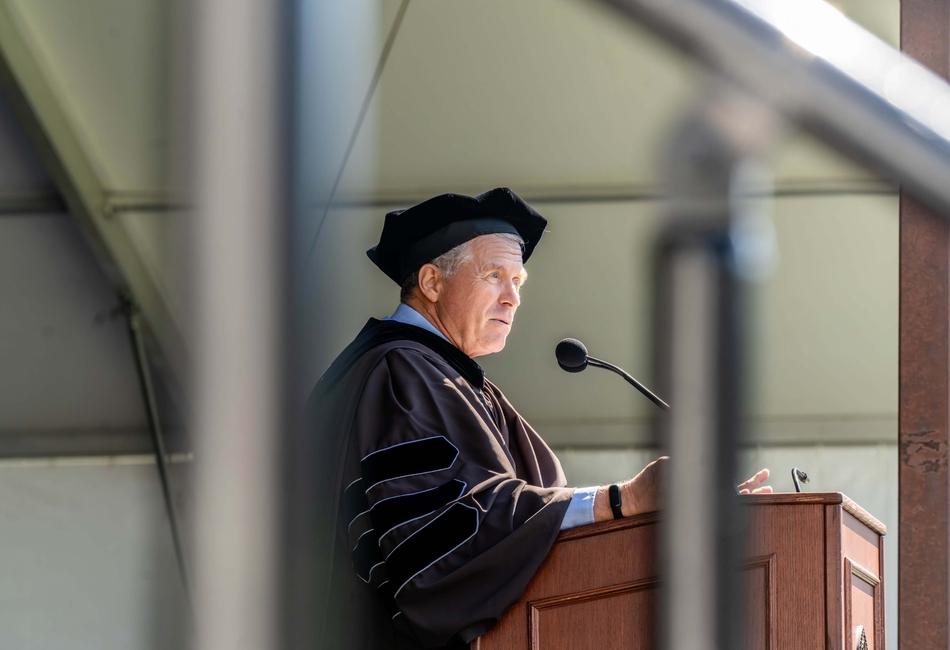 Photograph of Charlie Dent M'93 in academic regalia speaking at a podium.