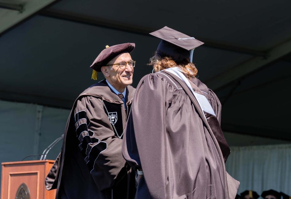Photograph of Lehigh President Joseph J. Helble '82 shaking hands with a graduate in academic regalia on stage.