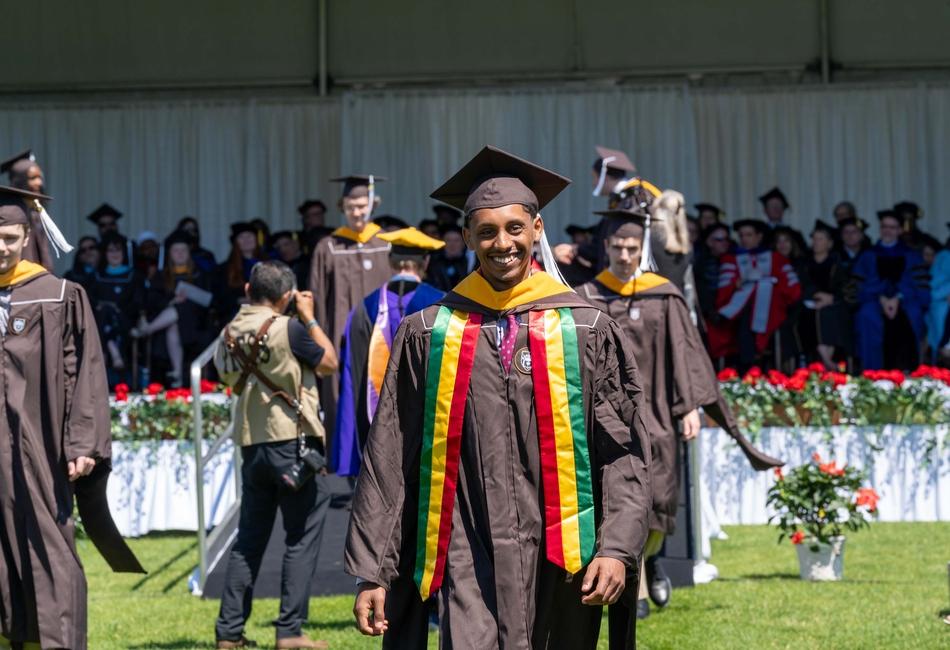 Photograph of a smiling graduate in brown regalia.