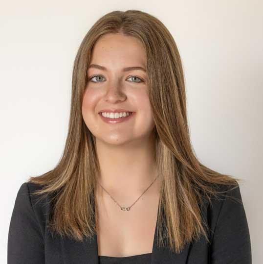 Photograph of a smiling young woman with long brown hair wearing a black blazer.