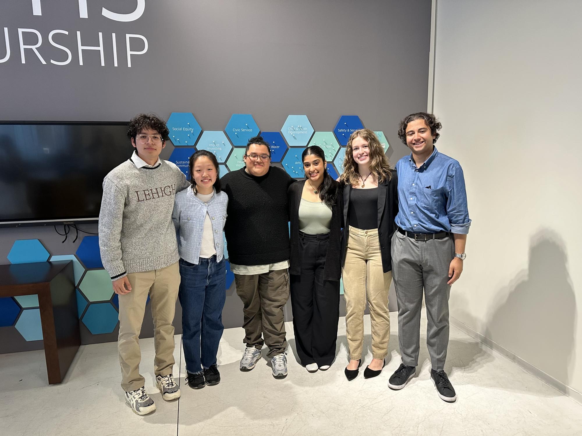 Photograph of six diverse young adults smiling in a modern office setting.
