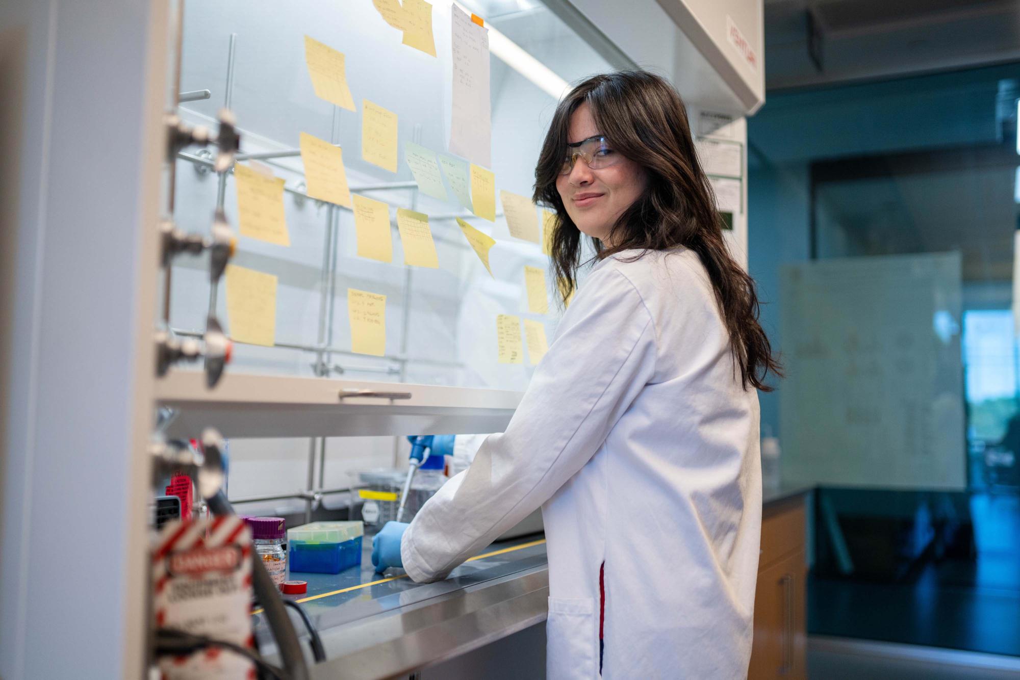 Photograph Lillian Wu in a white lab coat working at a fume hood.