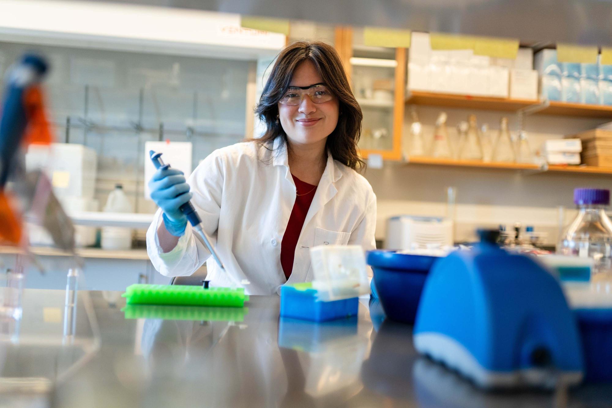 Photograph of Lillian Wu in a lab coat using a pipette in a laboratory.