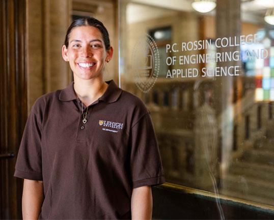 Photograph of Sydney Parlett '26 in a brown polo by the P.C. Rossin College of Engineering and Applied Science sign.