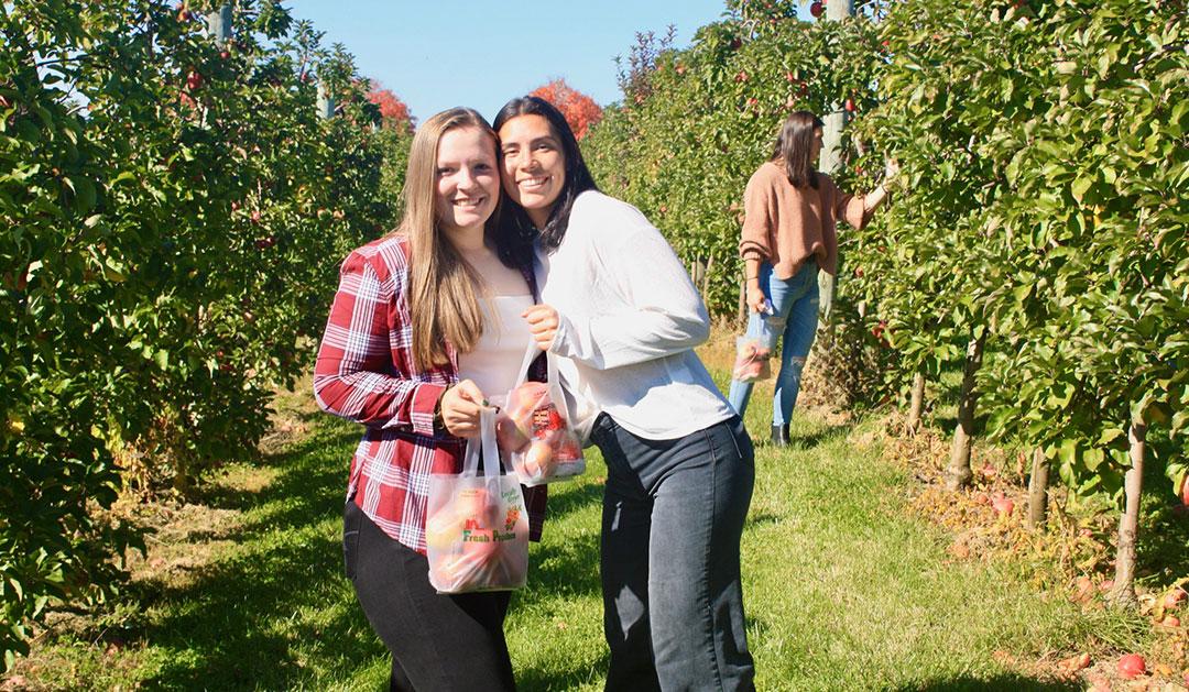 Photograph of Amanda Greaney '24 and Sydney Parlett '26 holding bags of apples in an orchard.