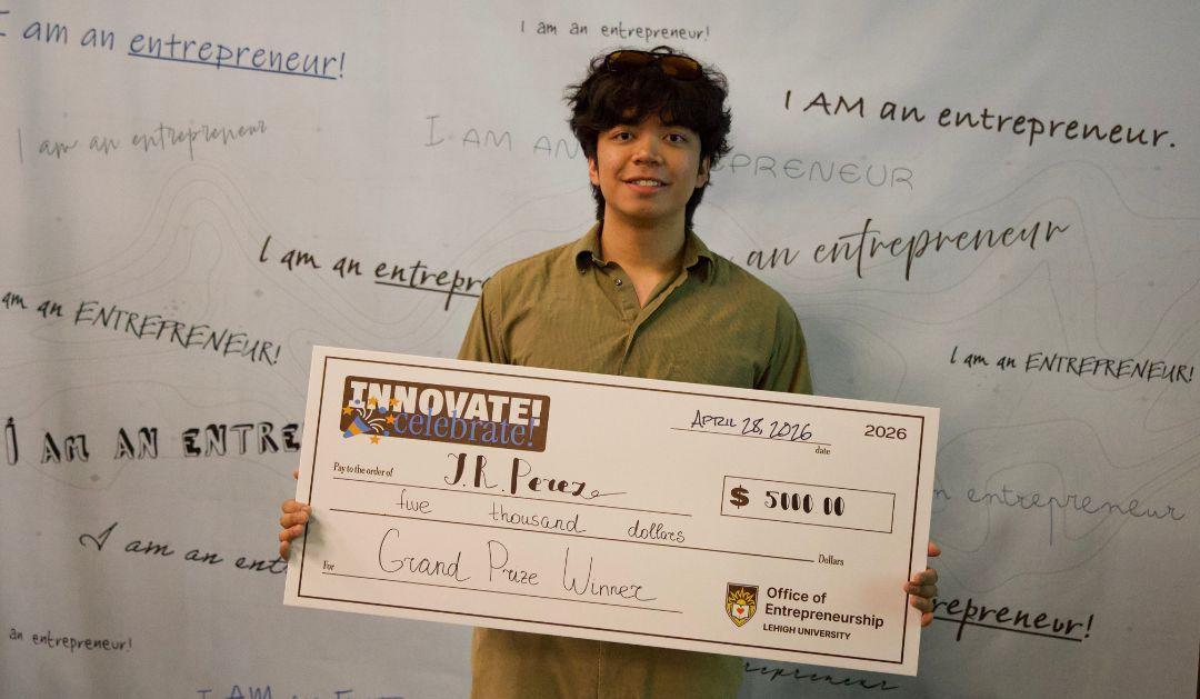Smiling young man holding a novelty check in front of an entrepreneur backdrop