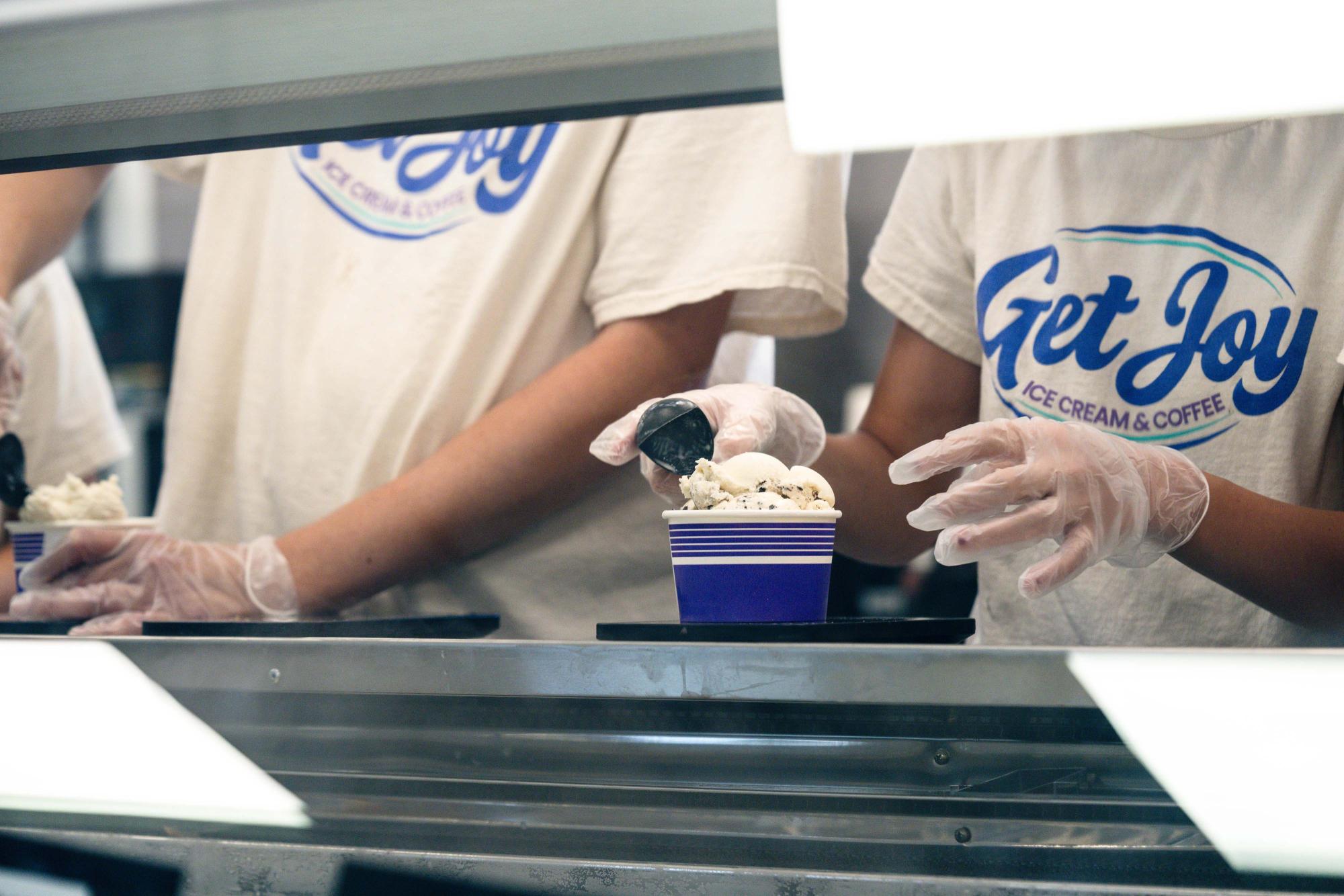Photograph of workers in "Get Joy" shirts scooping ice cream into purple cups.