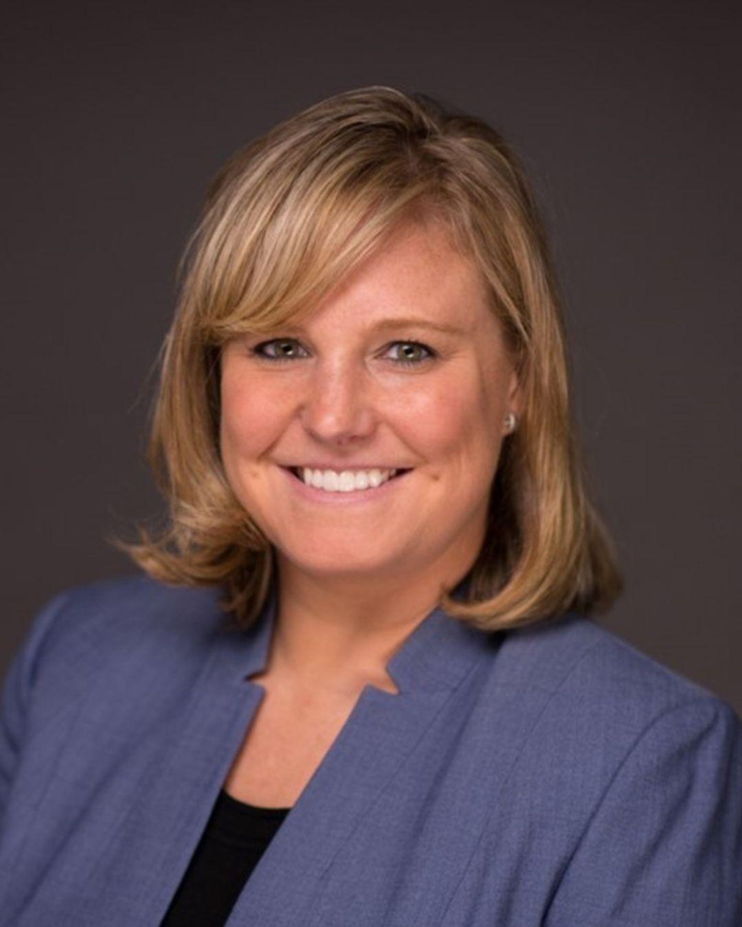 Professional photograph of a smiling blonde woman wearing a blue blazer.