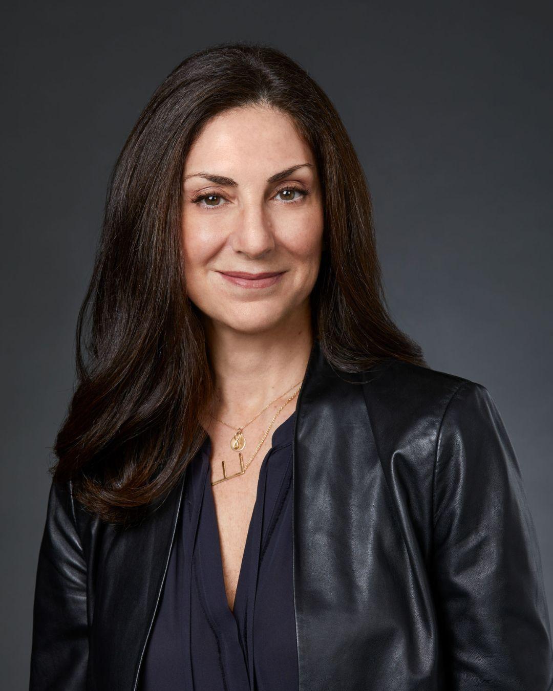 Photograph of a smiling woman with long brown hair wearing a black leather jacket.