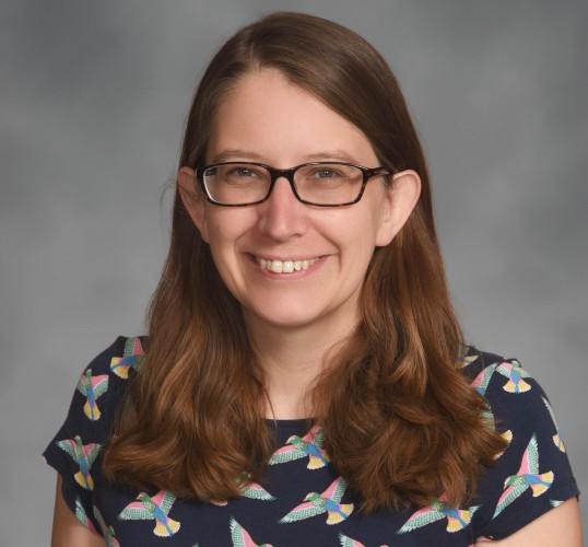 Professional headshot of woman with brown hair past her shoulders. She's smiling and has glasses.