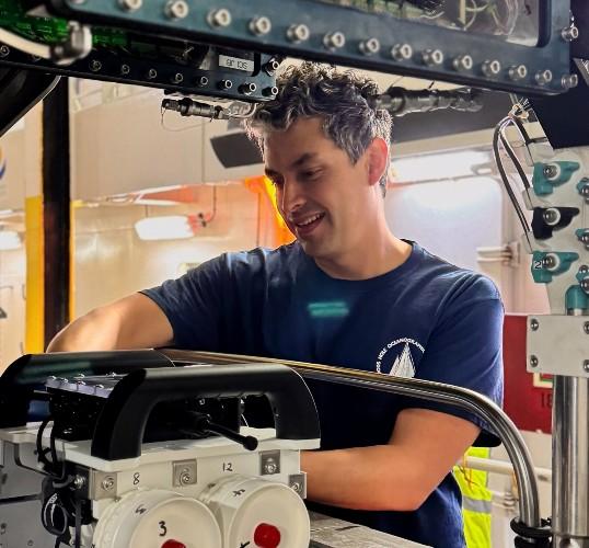 Photograph of a smiling man working on complex machinery.
