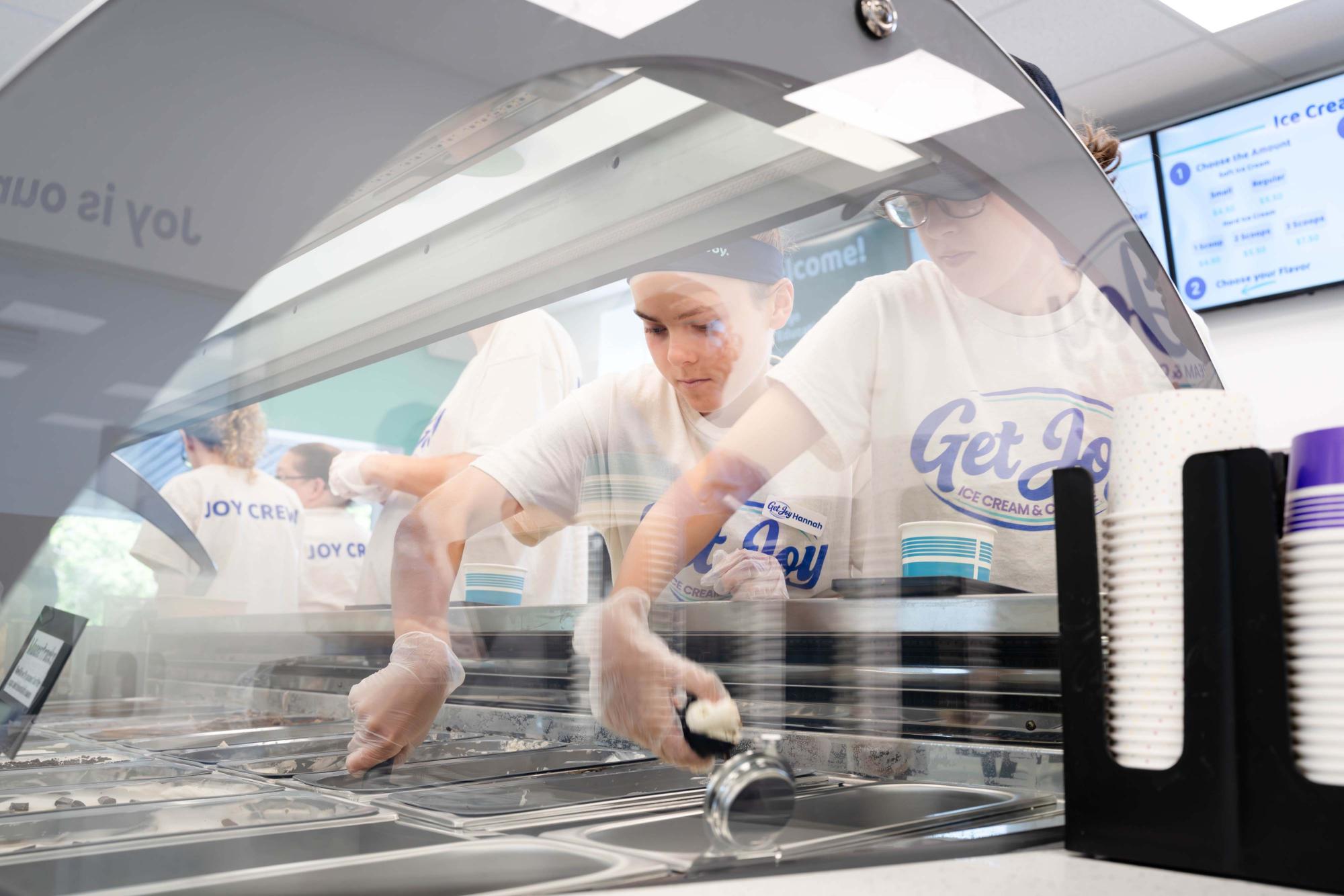 Photograph of staff in white t-shirts scooping gelato behind a glass display counter.