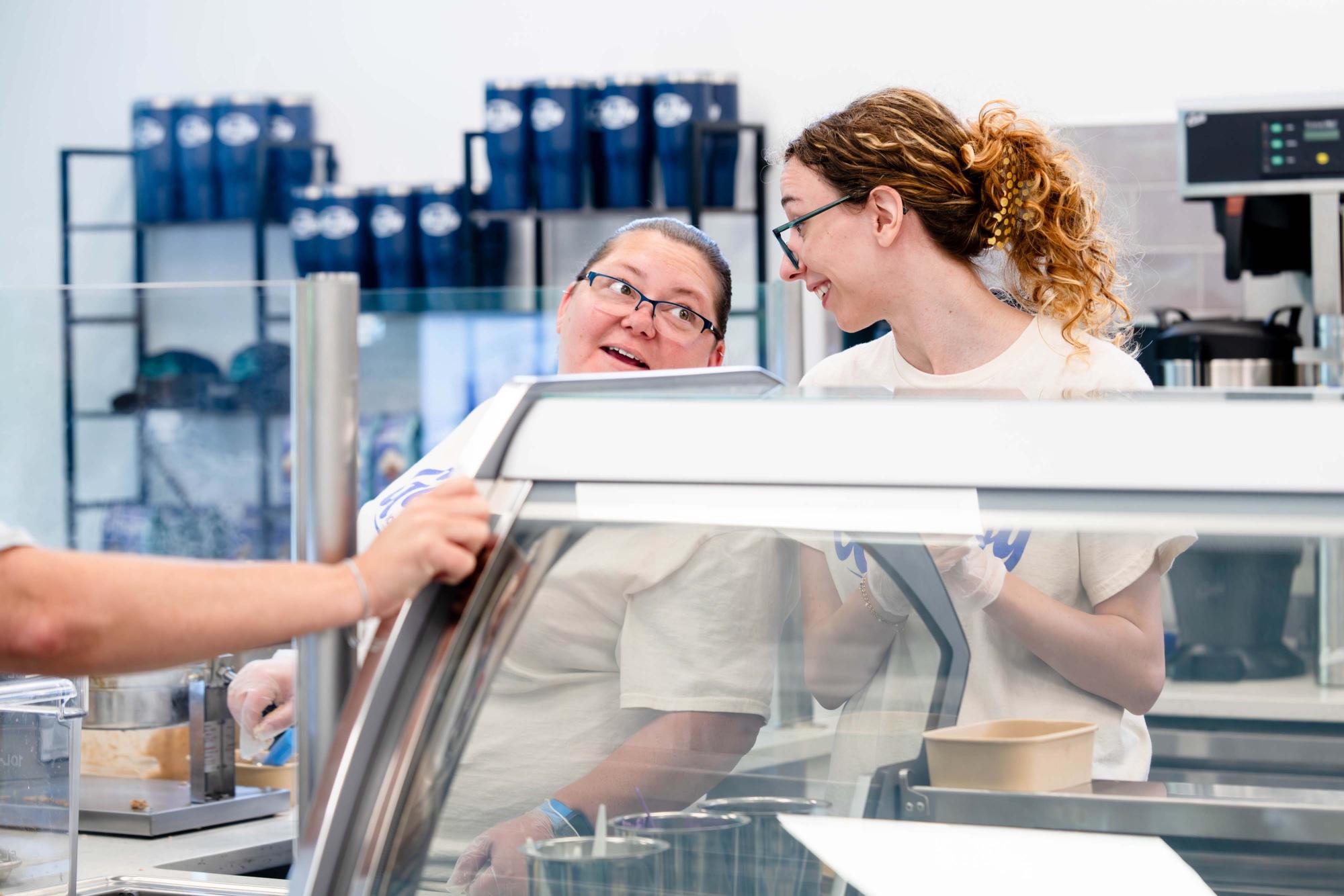 Photograph of two smiling food service workers interacting behind a counter.