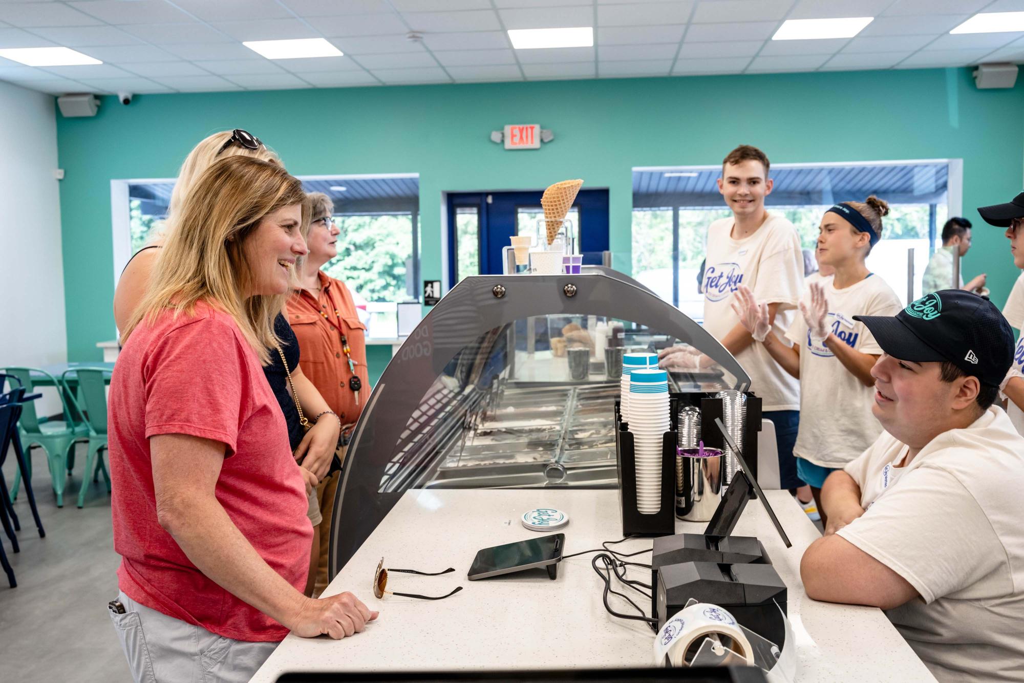 Photograph of smiling customers and staff at an ice cream counter.