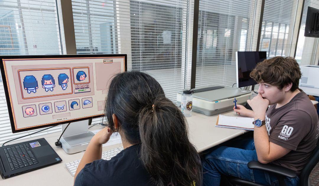 Photograph of two people working on digital character design in a computer lab.
